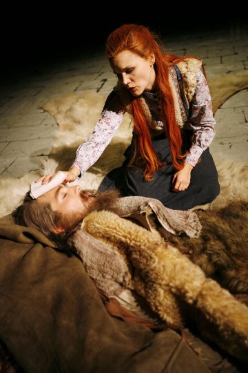 Pitkät punaiset hiukset omaava nainen polvistuu maassa makaavan parrakkaan miehen viereen ja laskee hellävaraisesti liinan hänen otsalleen. Molemmilla on maalaismaiset vaatteet, ja heidän ympärilleen on levitetty eläinten turkiksia. Ympäristö vaikuttaa dramaattiselta näyttämökuvaukselta.