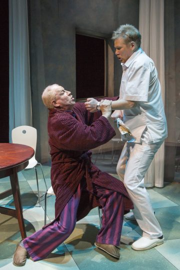 Lavalla esiintyy kaksi miestä; toinen heistä, jolla on aamutakki ja raidallinen pyjama, näyttää kamppailevan, kun toinen valkoisiin vaatteisiin pukeutunut mies, mahdollisesti sairaalan työntekijä, pitää häntä pystyssä minimaalisesti kalustetussa huoneessa.