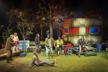 Seitsemän näyttelijää esiintyy metsäistä leirintäaluetta muistuttavassa lavastuksessa, jossa on suuri ränsistynyt asuntovaunu, puita, erilaisia tuoleja, laatikoita ja käsintehty suomenkielinen kyltti. Näyttämö on vilkas, näyttelijät ovat kesken toiminnan ja keskustelun.