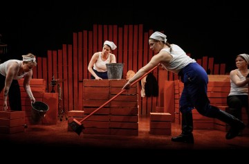 Lavalla esiintyy neljä valkoisiin toppiin, sinisiin housuihin ja huiviin pukeutunutta naista. He siivoavat ja työskentelevät ämpäreiden ja moppien kanssa punaisten laatikkopinojen ympäröimänä punaisella taustalla.