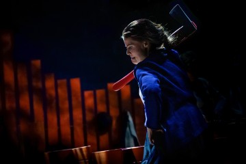 Siniseen asuun pukeutunut henkilö pitelee olallaan punaista kirvestä päättäväisen näköisenä, dramaattinen valaistus ja abstraktit punaiset muodot tummalla taustalla.