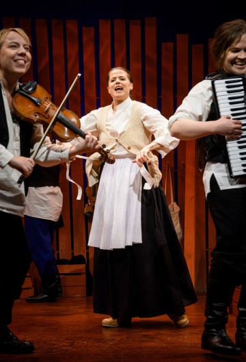 Lavalla kolme esiintyjää; yksi soittaa viulua, toinen harmonikkaa, kun taas keskimmäinen esiintyjä aikakauden puvussa laulaa intohimoisesti. Puupaneelit muodostavat taustan ja luovat lämpimän teatteriympäristön.