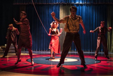 Viisi näyttelijää esiintyy näyttämöllä dramaattisessa valaistuksessa; yksi punamekkoon pukeutunut nainen seisoo keskellä pitelemässä hyppynarua, kun taas neljä muuta hyppii, ja kaikki tämä tapahtuu sinisten verhojen taustaa vasten.