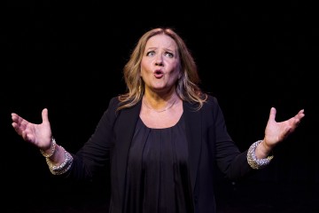 Mustiin vaatteisiin pukeutunut nainen seisoo mustaa taustaa vasten ja elehtii avosylin ja ilmeikkäin kasvoin, ikään kuin esiintyisi tai puhuisi intohimoisesti.