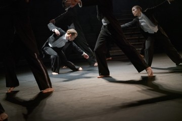 Neljä mustiin pukuihin ja valkoisiin paitoihin pukeutunutta tanssijaa esiintyy hämärästi valaistulla näyttämöllä, ja he esittävät dynaamisia, ilmeikkäitä asentoja taivutetuilla polvilla ja ojennetuilla käsillä, paljain jaloin tummalla lattialla.