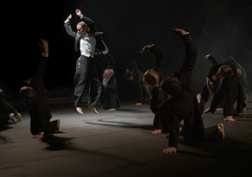 Lavalla esiintyy joukko tummiin pukuihin pukeutuneita tanssijoita; yksi tanssija hyppää dramaattisesti ilmaan, kun taas toiset poseeraavat matalalla maassa kädet ojennettuina, kaikki paljain jaloin dramaattisessa valaistuksessa.