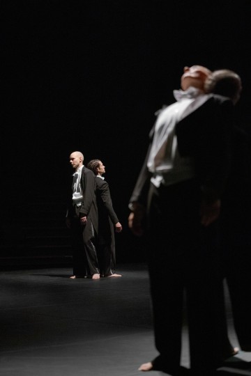 Neljä mustiin juhlapukuihin pukeutunutta ihmistä seisoo paljain jaloin hämärästi valaistulla näyttämöllä. Kaksi seisoo selkä toisensa takana taustalla, kun taas kaksi muuta on epäselvästi etualalla, heidän vartalonsa nojaavat ja päänsä kallistuvat ylöspäin.