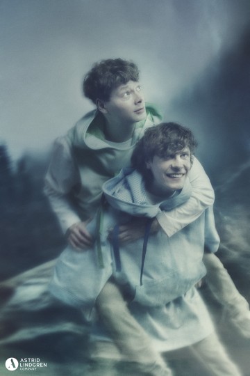 Ulkona on kaksi nuorta miestä vaaleissa keskiaikaisissa hupullisissa tunikoissa. Toinen antaa toiselle hevoskyytiä; molemmat näyttävät iloisilta. Kohtaus on pehmeän unenomainen, ja siinä on sumea metsätausta ja Astrid Lindgrenin logo kulmassa.