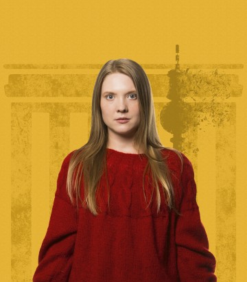 Pitkät vaaleat hiukset omaava nainen, jolla on punainen villapaita, seisoo keltaisen taustan edessä, ja hänen takanaan on heikko, tyylitelty kuva klassisesta rakennuksesta.