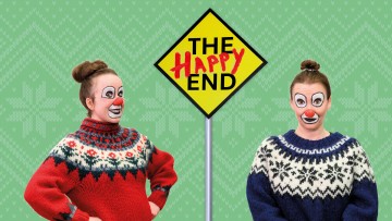 Kaksi klovni-meikattua ja juhlapaitaista naista seisoo keltaisen kyltin molemmin puolin, jossa lukee THE HAPPY END ja punaisella käsin kirjoitettu HAPPY vihreällä kuviotaustalla.