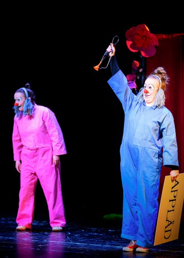 Lavalla esiintyy kaksi värikkäisiin haalareihin pukeutunutta klovnia. Sinipukuinen klovni pitää kädessään pientä torvea ja keltaista kylttiä, jossa lukee 