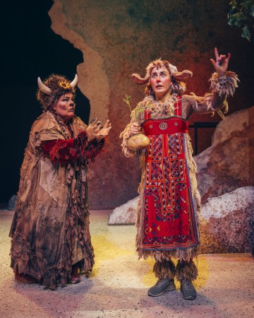 Lavalla seisoo kaksi näyttelijää taidokkaissa, sarvipäisissä puvuissa. Toisella on turkisviitta ja sarvipäinen hattu, toisella punakuvioinen esiliina ja hänellä on kädessään kurpitsa, jossa on kasvi, ja hän elehtii dramaattisesti. Taustalla on kallioinen ympäristö.