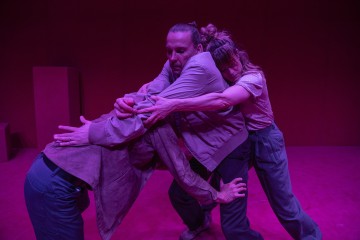 Kolme satunnaisesti pukeutunutta ihmistä kietoutuu toisiinsa dramaattisessa poseerauksessa vaaleanpunaisella valaistulla näyttämöllä, ja jokainen heistä kurottautuu ja pitää kiinni toisesta voimakkain ilmein, jotka välittävät tunteita ja yhteyttä.