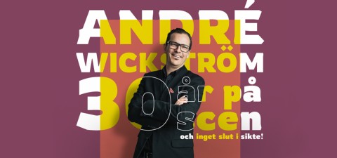 Silmälasipäinen pukumies seisoo hymyillen ja kädet ristissä värikkään tekstin edessä, jossa lukee: André Wickström 30 år på scen och inget slut i sikte! ruskealla pohjalla.
