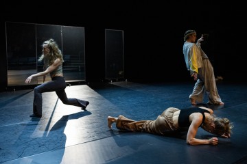 Kolme nykytanssijaa esiintyy hämärästi valaistulla näyttämöllä. Yksi tanssija on matalalla maassa, toinen on keskellä askelta ja toinen nojaa dramaattisesti taaksepäin. Taustalla on heijastavia paneeleita.