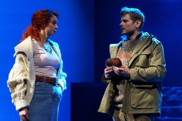 Punaiset kiharat hiukset omaava nainen ja vaaleanruskeat hiukset omaava mies seisovat vastakkain sinisessä näyttämövalaistuksessa. Naisella on kermanvärinen pusero ja farkkuhame; miehellä on vihreä takki ja hänellä on kädessään kaksi lankakerää.