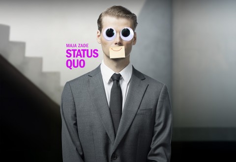 Harmaaseen pukuun pukeutunut mies, jolla on karikatyyrimäiset silmät ja tarralappu hymynaama, seisoo modernin portaikon edessä. Lihavoitu vaaleanpunainen teksti kuuluu: MAJA ZADE STATUS QUO.