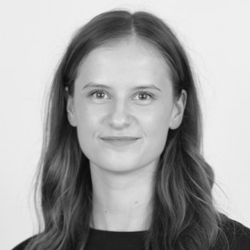 Nuori nainen, jolla on pitkät, suorat hiukset, hymyilee pehmeästi ja katsoo suoraan kameraan. Hänellä on yllään tumma toppi, ja tausta on tavallinen ja vaalea. Kuva on mustavalkoinen.