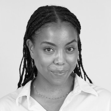 Mustavalkoinen muotokuva naisesta, jolla on punotut hiukset, vaalea napillinen paita ja hento kaulakoru, ja joka katsoo suoraan kameraan hennosti hymyillen.