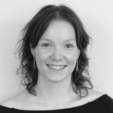 Nuori nainen, jolla on aaltoilevat, olkapään mittaiset tummat hiukset, hymyilee kameralle. Kuva on mustavalkoinen.