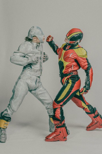 Kaksi futuristisiin, värikkäisiin asuihin pukeutunutta ihmistä poseeraa kuin lavastetussa taistelussa; toisella on hopeinen puku ja kypärä, toisella punainen, musta ja keltainen puku ja vastaava kypärä, ja hän nostaa nyrkkiä vastustajaa kohti.