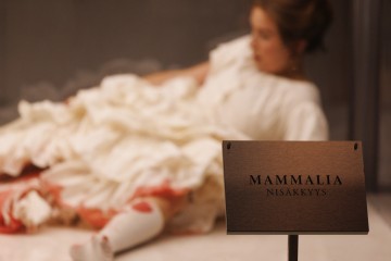 Taustalla makaa epäselvä hahmo valkoisessa mekossa, kun taas etualalla teräväpiirteisessä kyltissä lukee ”Mammalia Nisäkkäys…”.