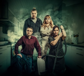 Neljä ihmistä poseeraa vakavana dramaattisen savun täyttämässä keittiössä. Yksi nainen polvistuu pölynimuri kädessään, kun kolme muuta seisovat tiiviisti hänen takanaan ja katsovat kaikki suoraan kameraan.