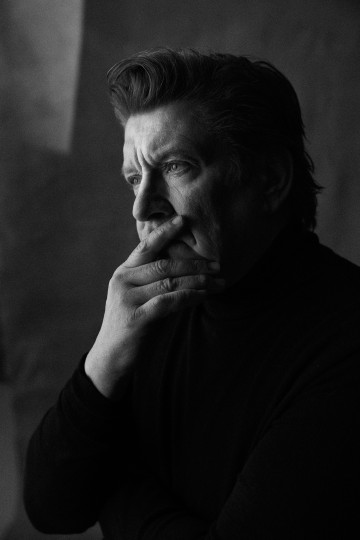 Mustaan poolokaulukseen pukeutunut mies seisoo profiilissa, nostaa kätensä suulleen ja katsoo mietteliäästi kaukaisuuteen. Kuva on mustavalkoinen, ja dramaattinen valaistus korostaa miehen mietteliästä ilmettä.